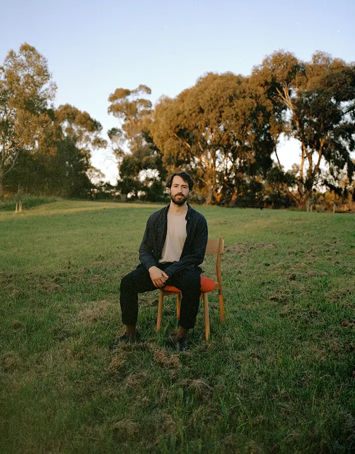 Designer James Walsh sitting on Charlie Dining chair in green field