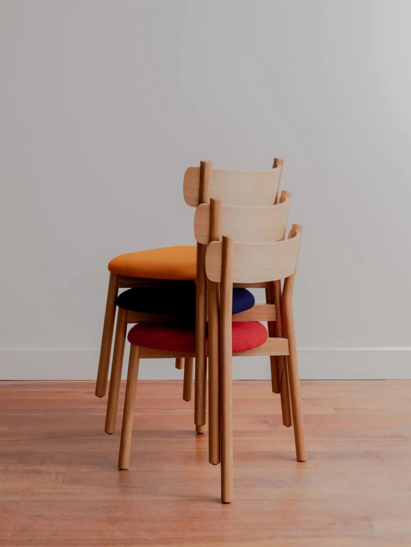 American Oak charlie dining chairs stacked three high, with red, blue and yellow upholstered seat pads