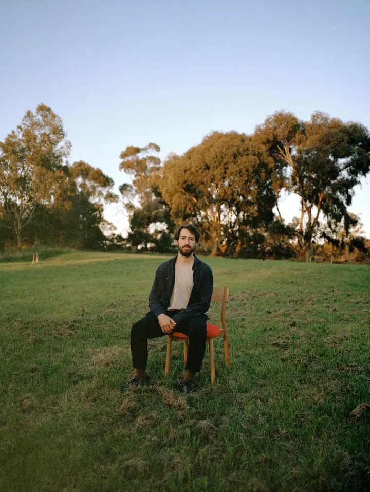 Designer James Walsh sitting on Charlie Dining chair in green field