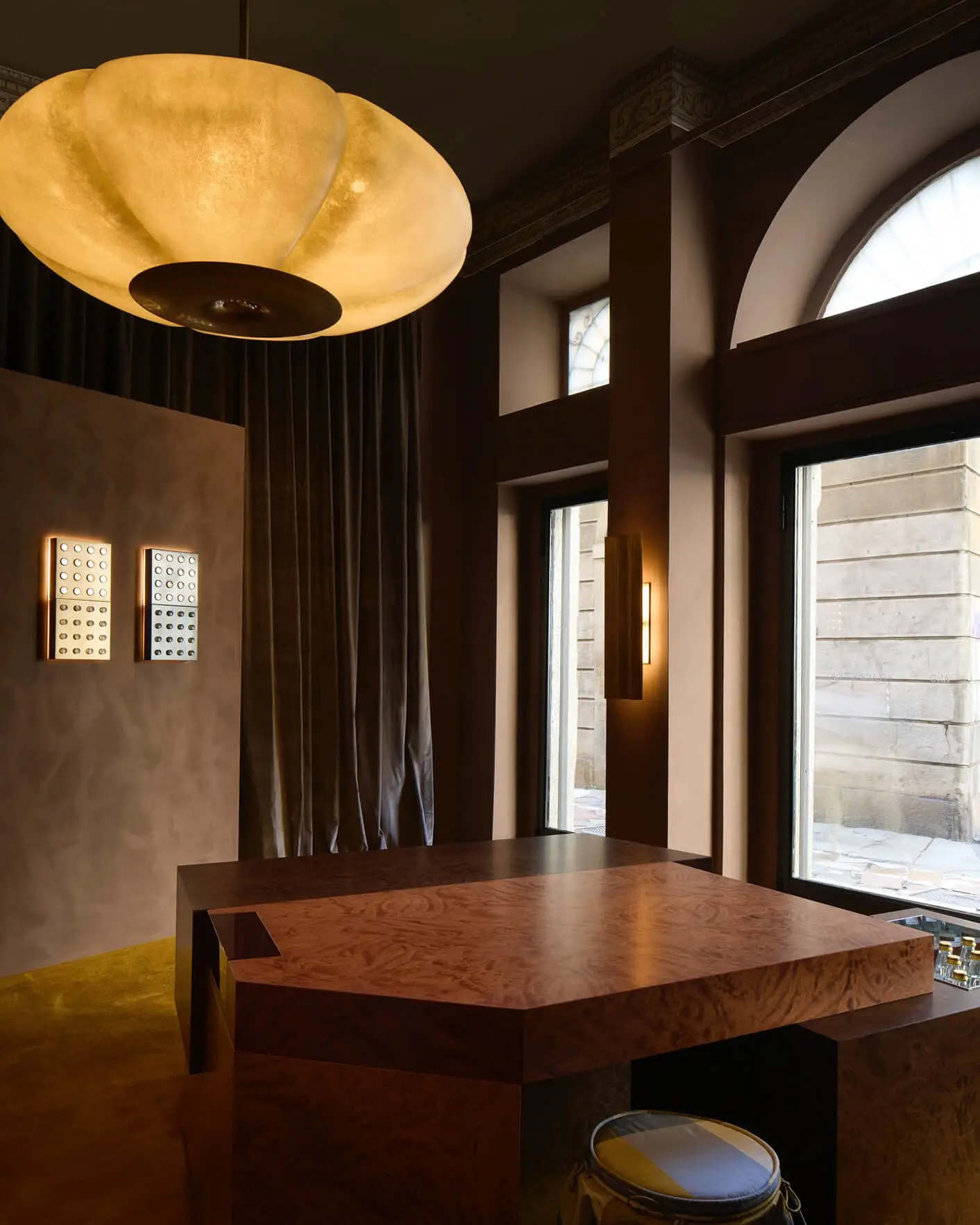 Dark and moody interior space from an exhibition in Milan with large fiber glass pendant lights with brass detailing, along with rich timber finishes